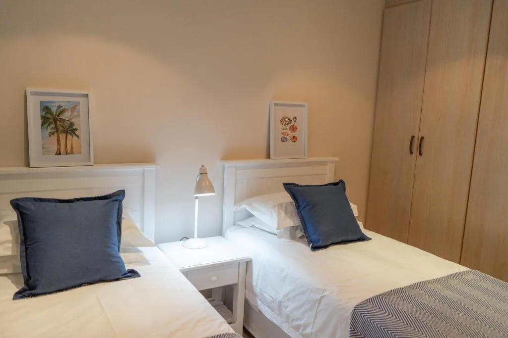 Twin bedroom with navy pillows, white bedding, wooden wardrobe, and framed artwork
