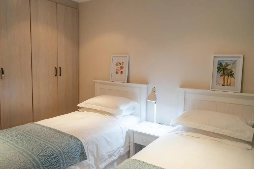 Twin bedroom with white bedding, wooden wardrobes, and botanical wall art