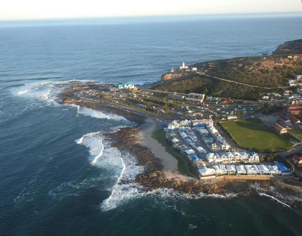 Aerial view of coastal town with crashing waves and lighthouse in distance