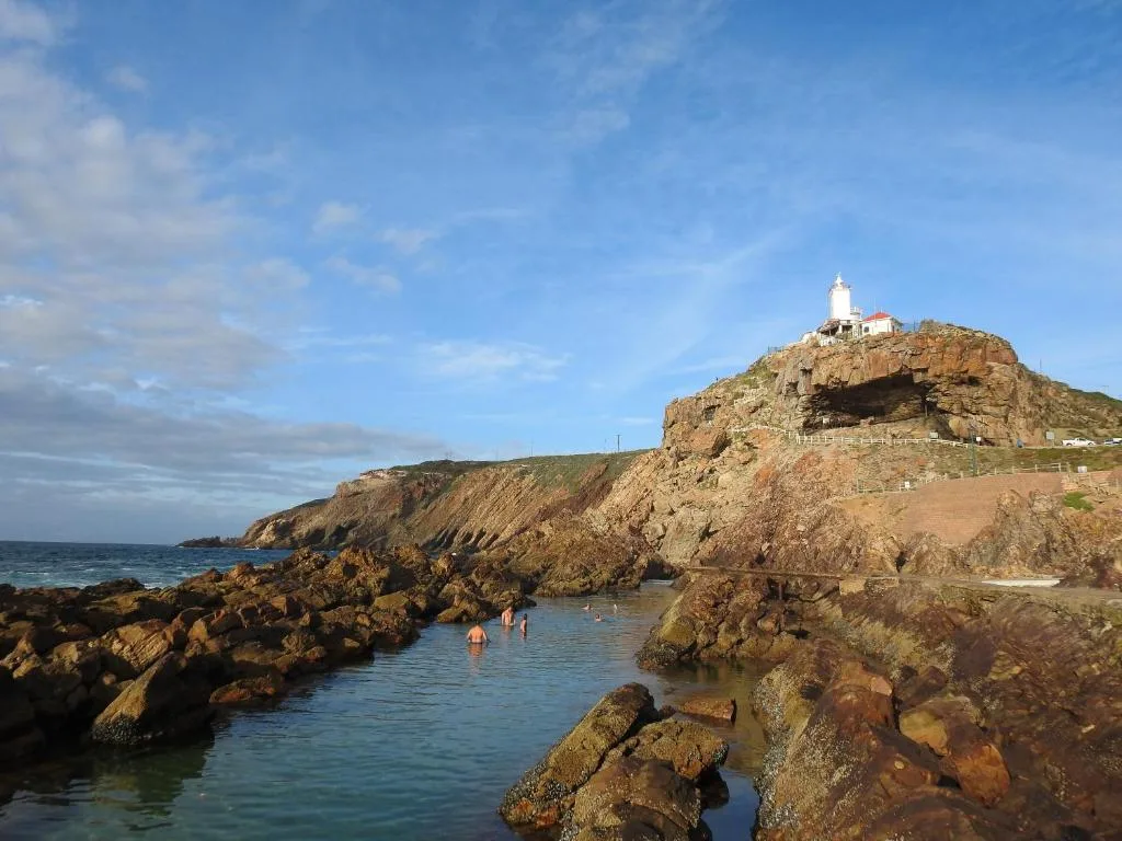 Scenic coastal landscape with lighthouse, rocky cliffs, and blue ocean water