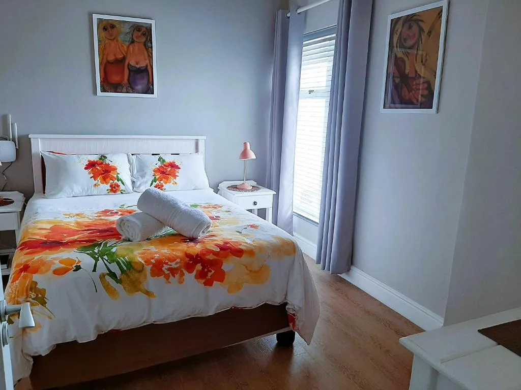 Bright bedroom with floral bedding, white nightstand, and glass doors