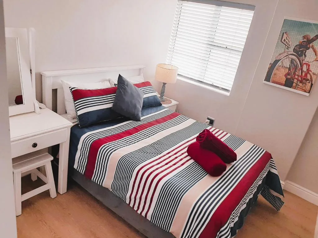 Bright bedroom with striped red and navy bedding, white furniture, and window
