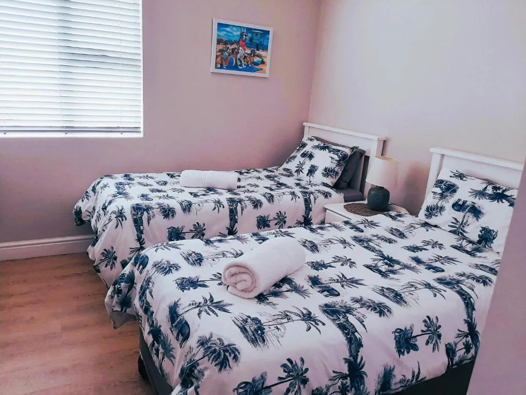 Twin bedroom with pink walls, palm-print bedding, and wooden floors