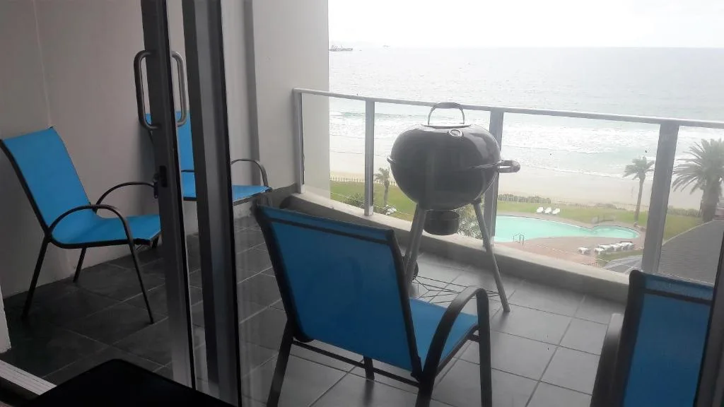 Beachfront balcony with blue chairs, braai grill, and ocean view