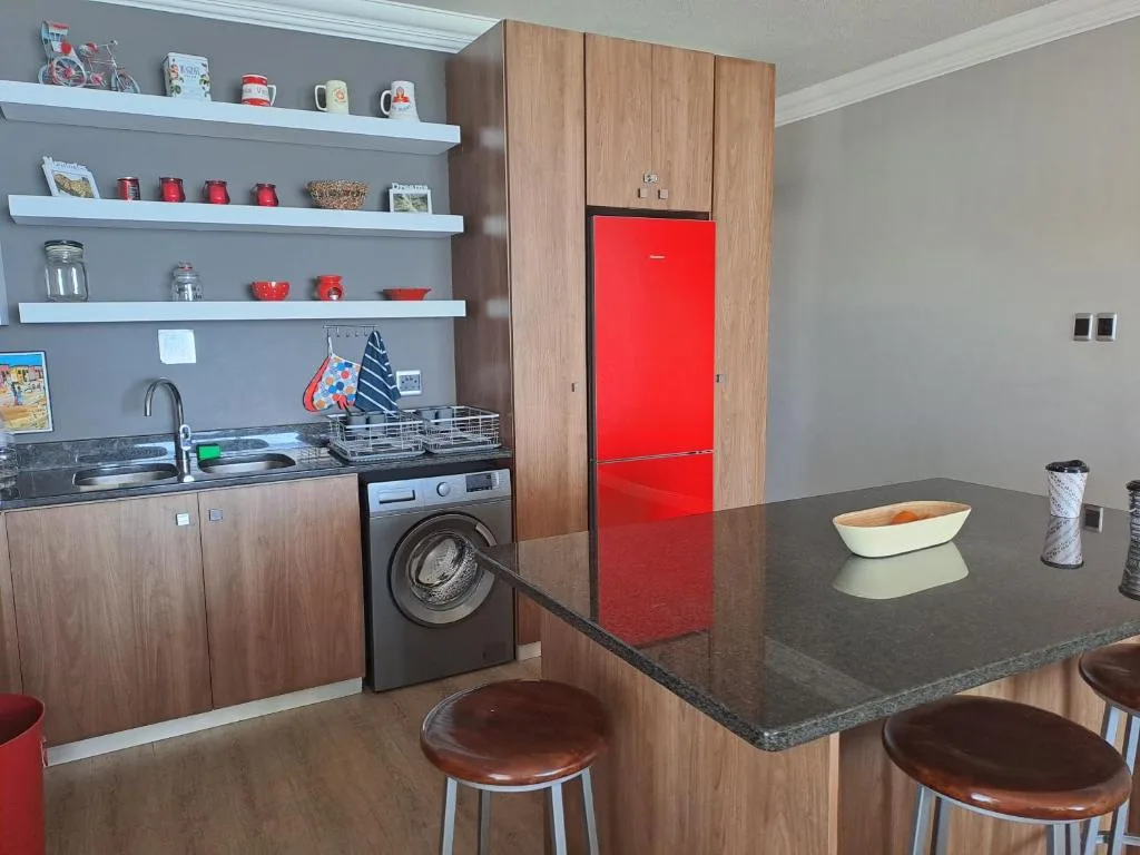 Modern kitchen with red fridge, washing machine, dark countertop and wooden cabinetry