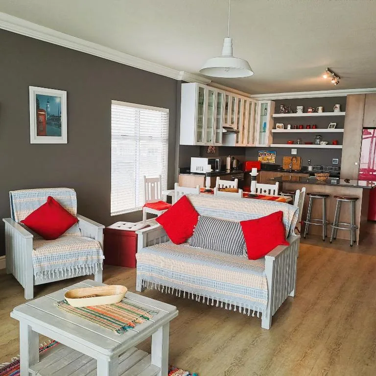 Open-plan lounge with white furniture, red cushions, and kitchen visible