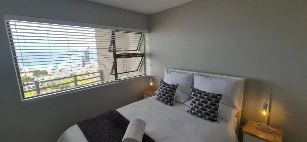 Modern bedroom with queen bed, geometric pillows, and large window overlooking coastal area