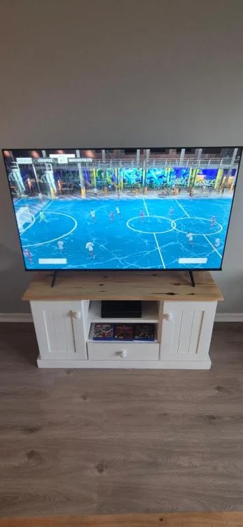Living room with wall-mounted TV displaying sports game, white cabinet