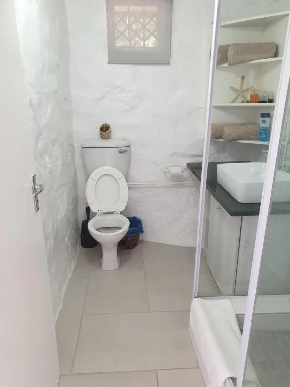Clean white bathroom with toilet, sink, and open shelving storage