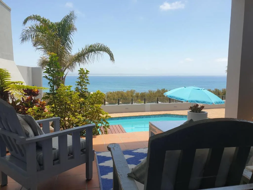 Oceanview deck with pool, lounge chairs, and turquoise umbrella