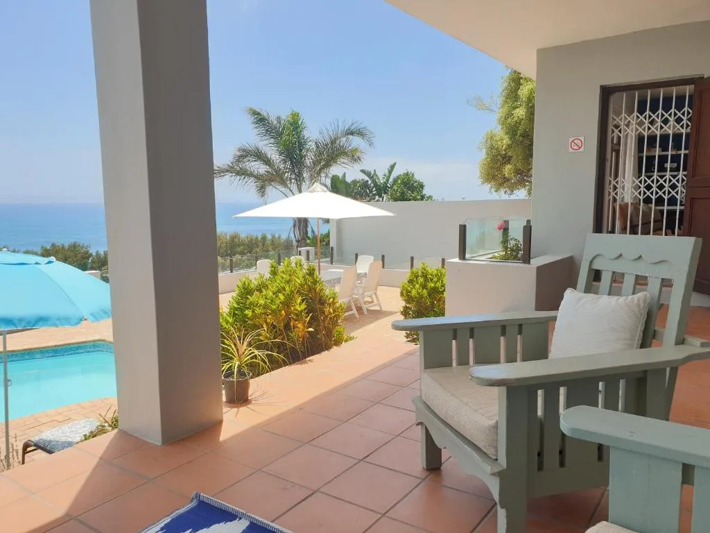 Spacious patio with seating, umbrella, pool and ocean view beyond