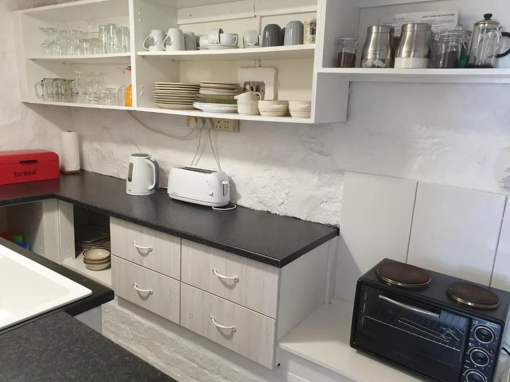 Compact kitchen with white cabinetry, black countertop, open shelving, and appliances