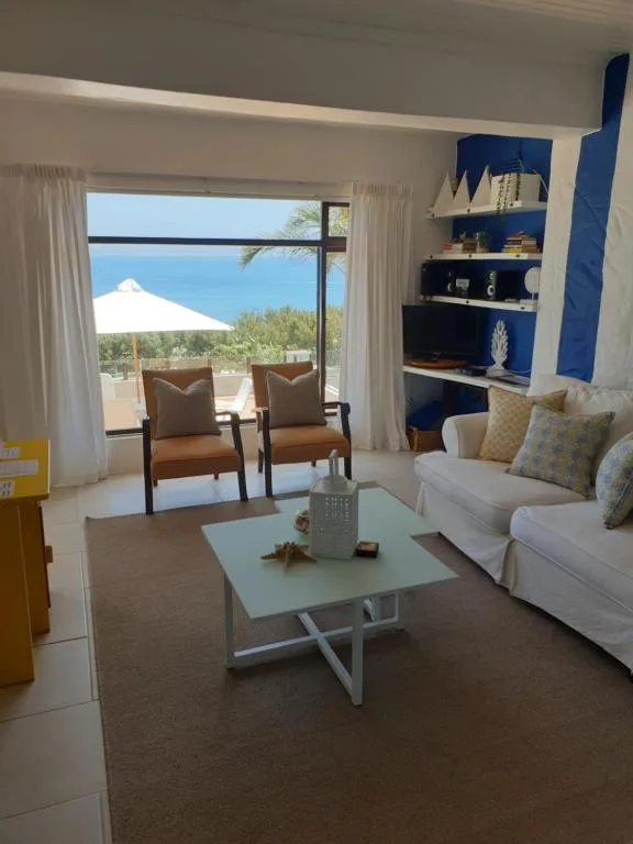 Bright lounge with ocean view, sofa, armchairs, and coastal decor shelving