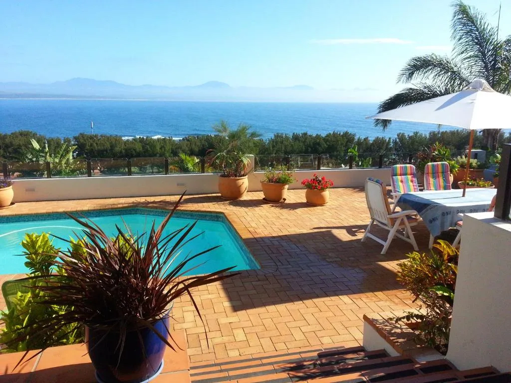 Swimming pool with ocean view, loungers, and tropical garden surroundings