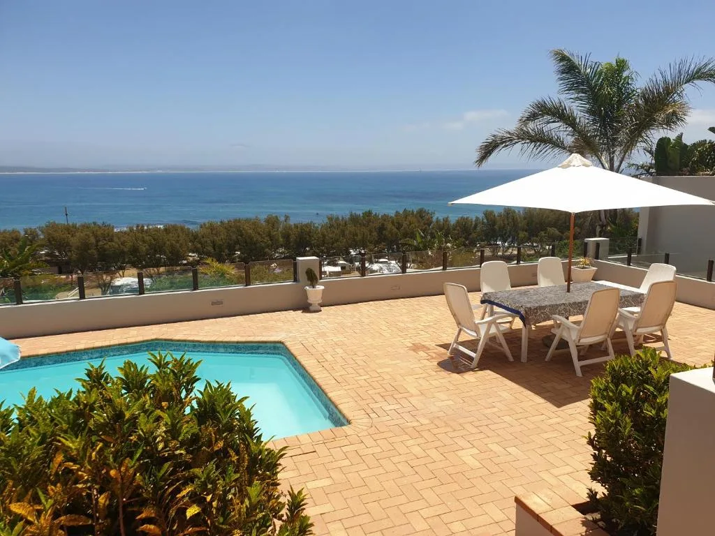 Swimming pool and patio with ocean view, umbrella, and dining furniture