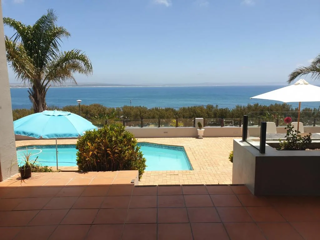 Swimming pool with ocean view, umbrellas, and coastal landscape beyond