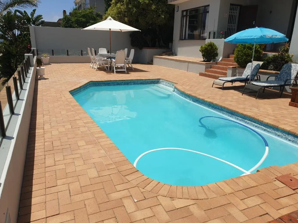 Sparkling blue swimming pool with loungers and umbrellas on terracotta deck