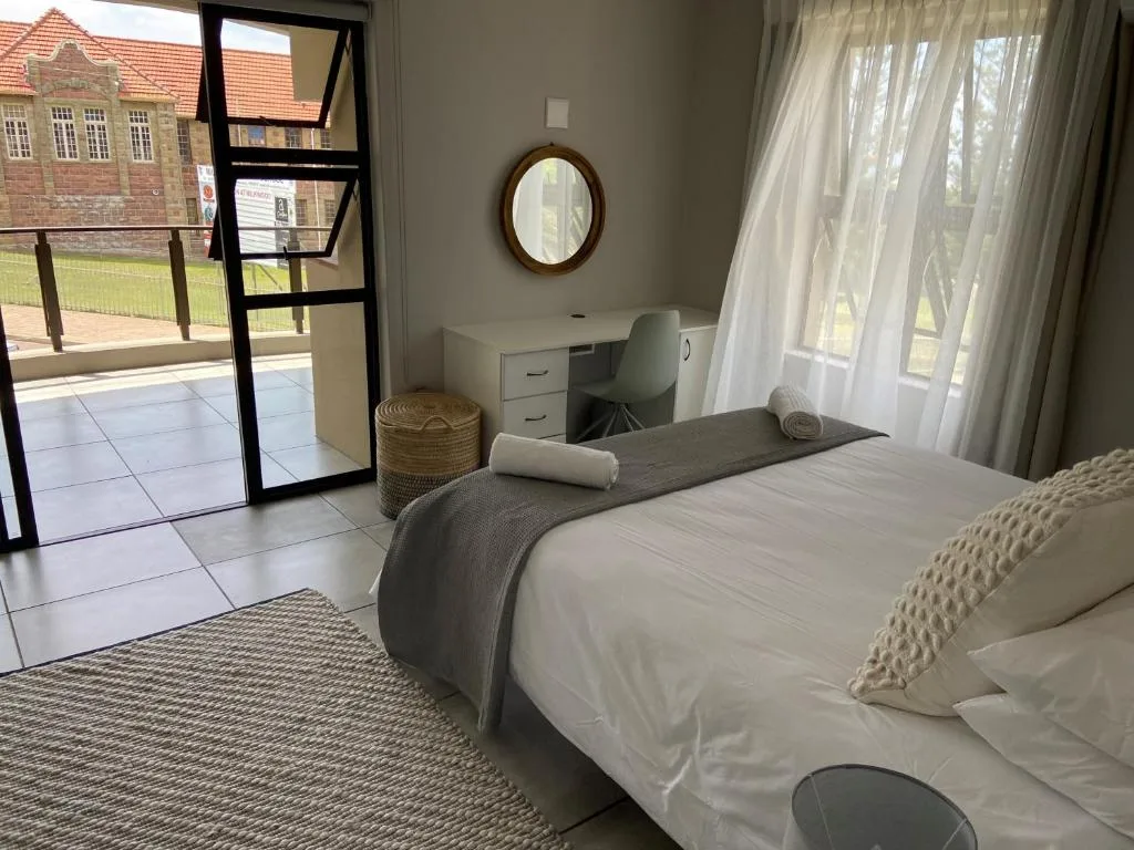 Bright bedroom with white bedding, work desk, and patio access overlooking gardens
