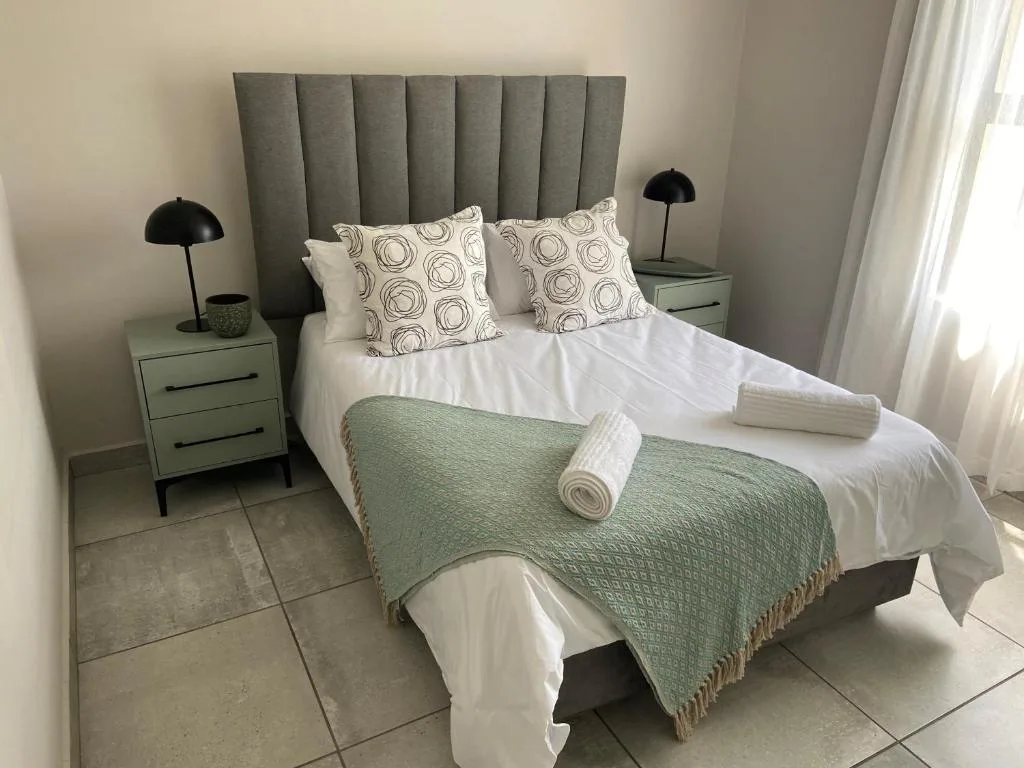 Modern bedroom with grey upholstered headboard and white bedding with green throw