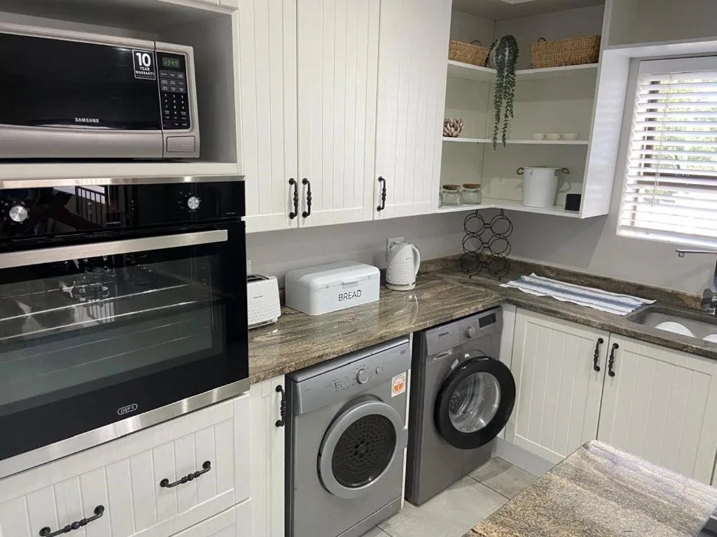 Modern kitchen with white cabinetry, granite counters, built-in appliances and washing machines