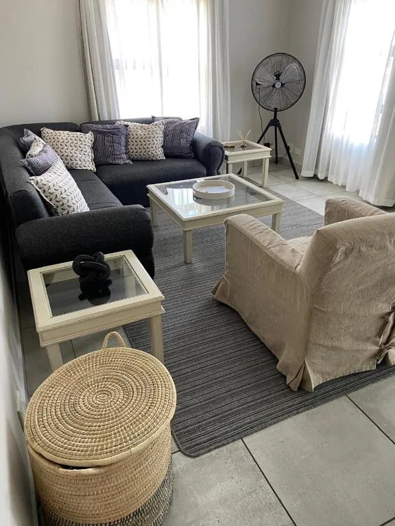 Spacious lounge with dark sectional sofa, cream armchair, and natural light from windows