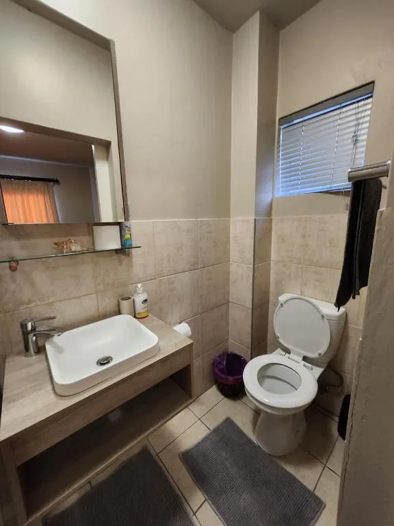 Bathroom with white sink, toilet, tiled walls, and mirror