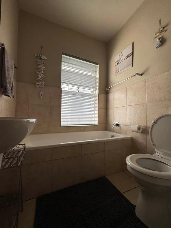 Bathroom with bathtub, toilet, sink, and window with blinds