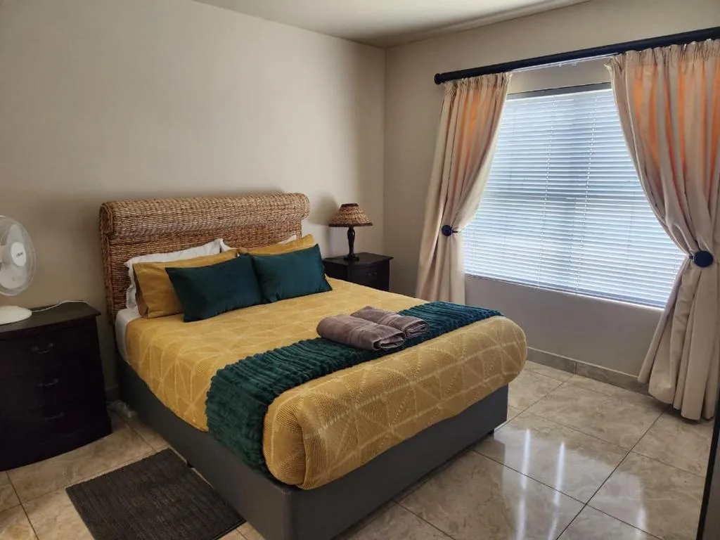 Spacious bedroom with queen bed, yellow bedding, green pillows, and large windows