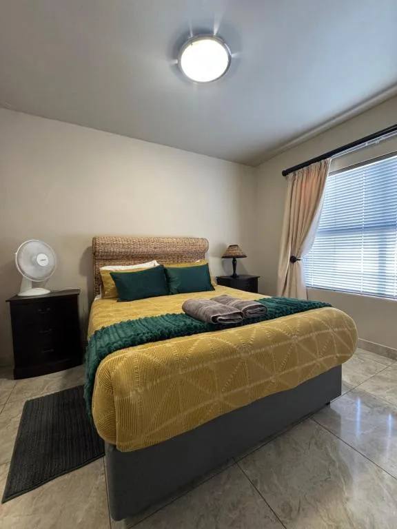 Bright bedroom with yellow and green bedding, wicker headboard, and natural light