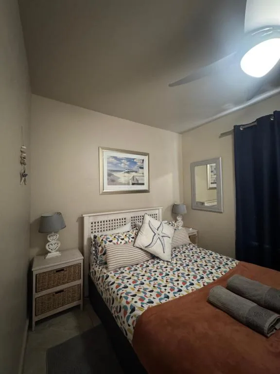 Bright bedroom with patterned bedding, wooden nightstand, and framed artwork