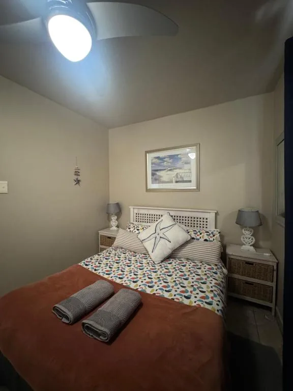 Cozy bedroom with patterned bedspread, decorative pillows, and coastal artwork