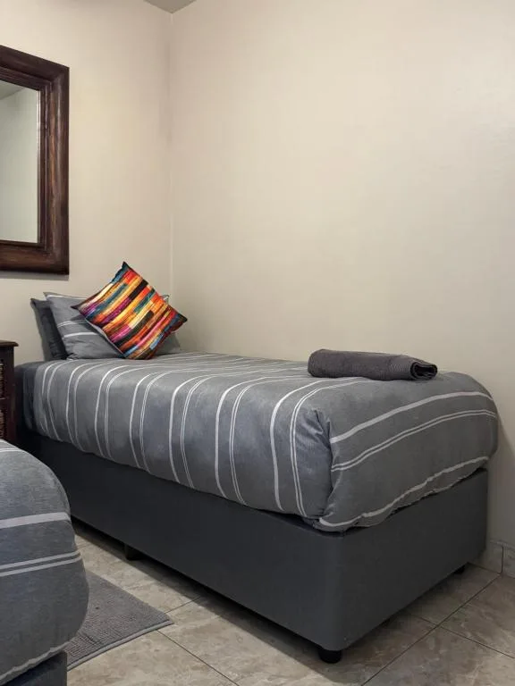 Single bed with striped grey duvet and colorful accent pillow in bedroom