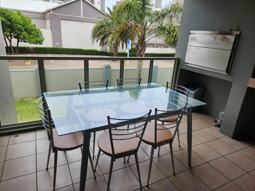 Glass-topped dining table with chairs on covered patio overlooking garden