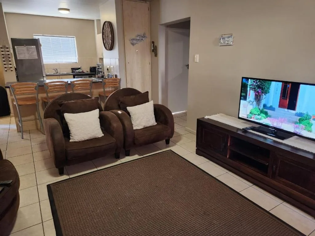 Open-plan lounge with brown leather sofas, flat-screen TV, and kitchen area visible