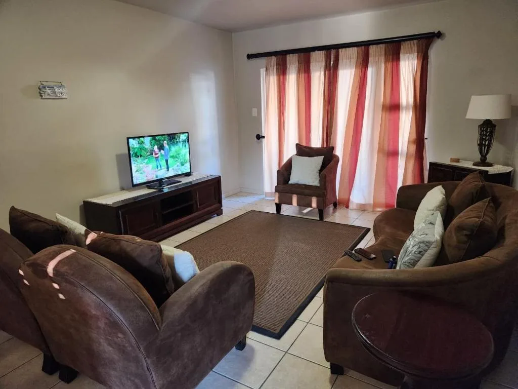 Spacious living room with brown sofas, TV, and striped curtains opening to patio