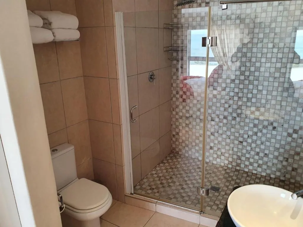 Spacious bathroom with walk-in shower, toilet, and rolled towels on rack