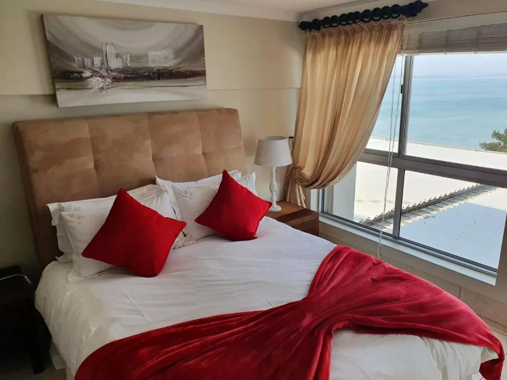 Bright bedroom with ocean view, red pillows, and large windows overlooking the sea