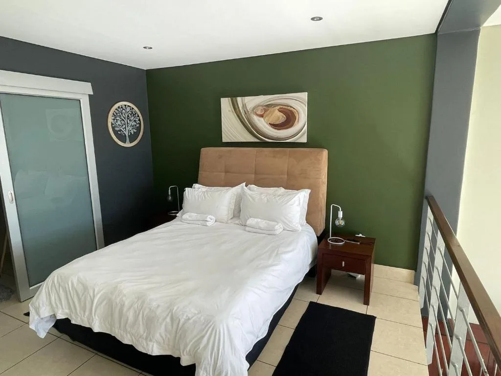 Contemporary bedroom with green walls, tan headboard, white linens, and artwork