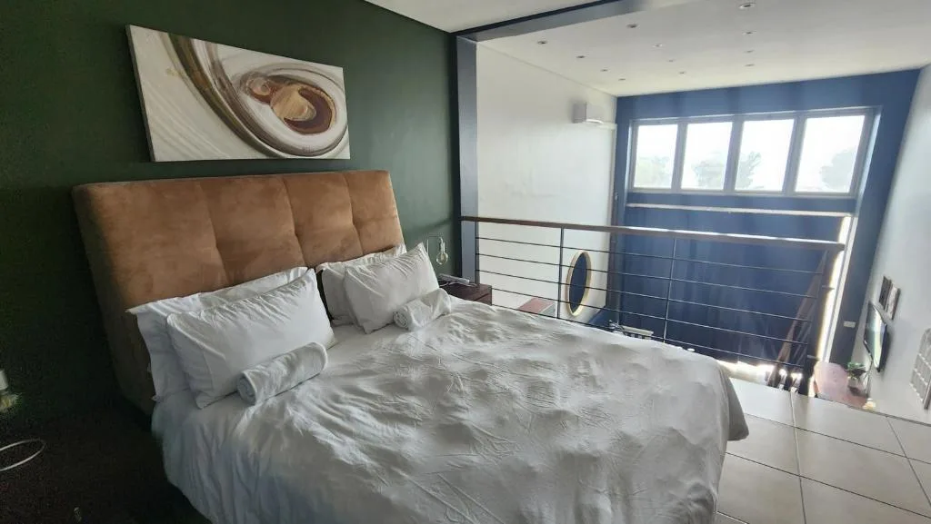 Modern bedroom with brown upholstered headboard, white bedding, green walls, and blue doors