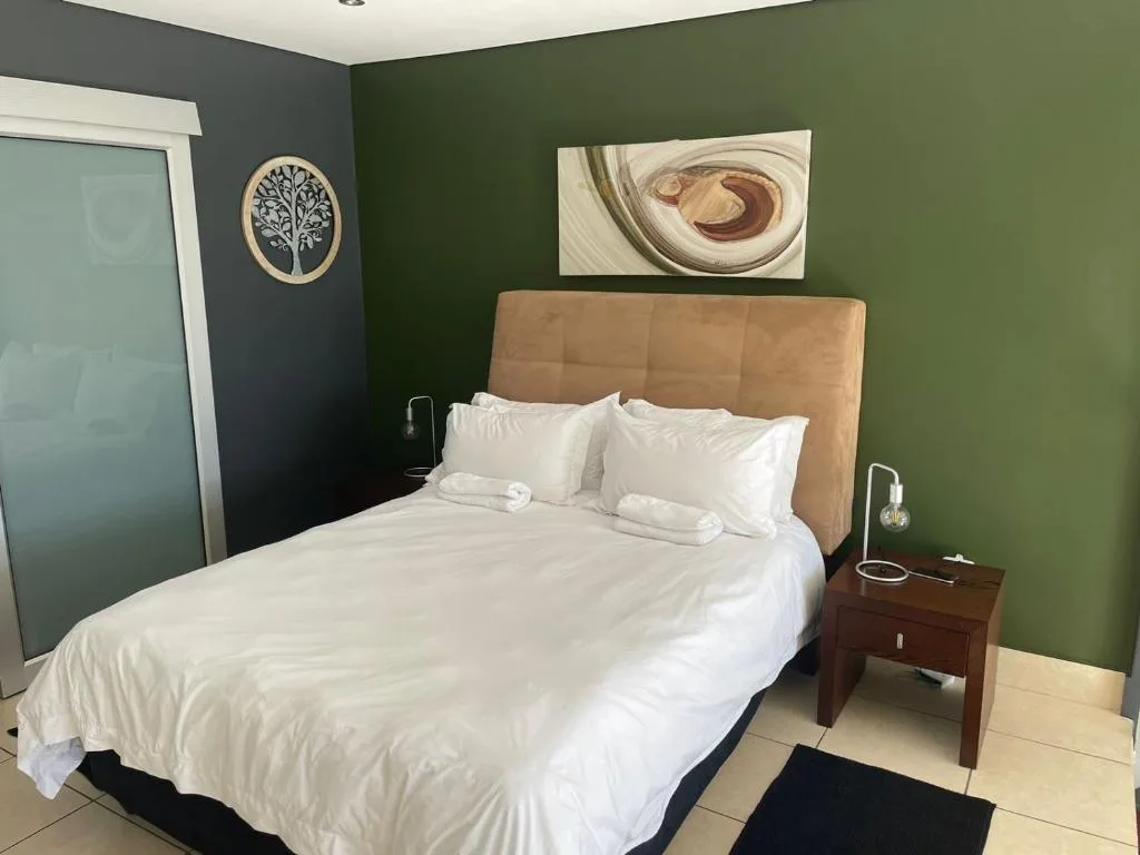 Modern bedroom with tan headboard, white bedding, and green accent walls