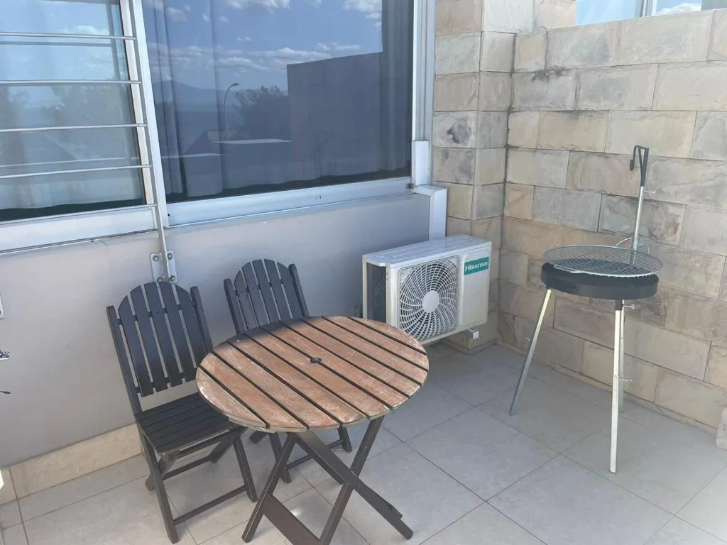 Small outdoor patio with wooden table, two chairs, and braai grill