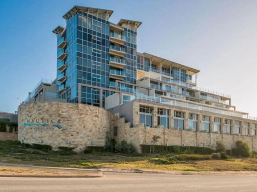 Modern multi-story beachfront apartment building with stone base and blue glass tower