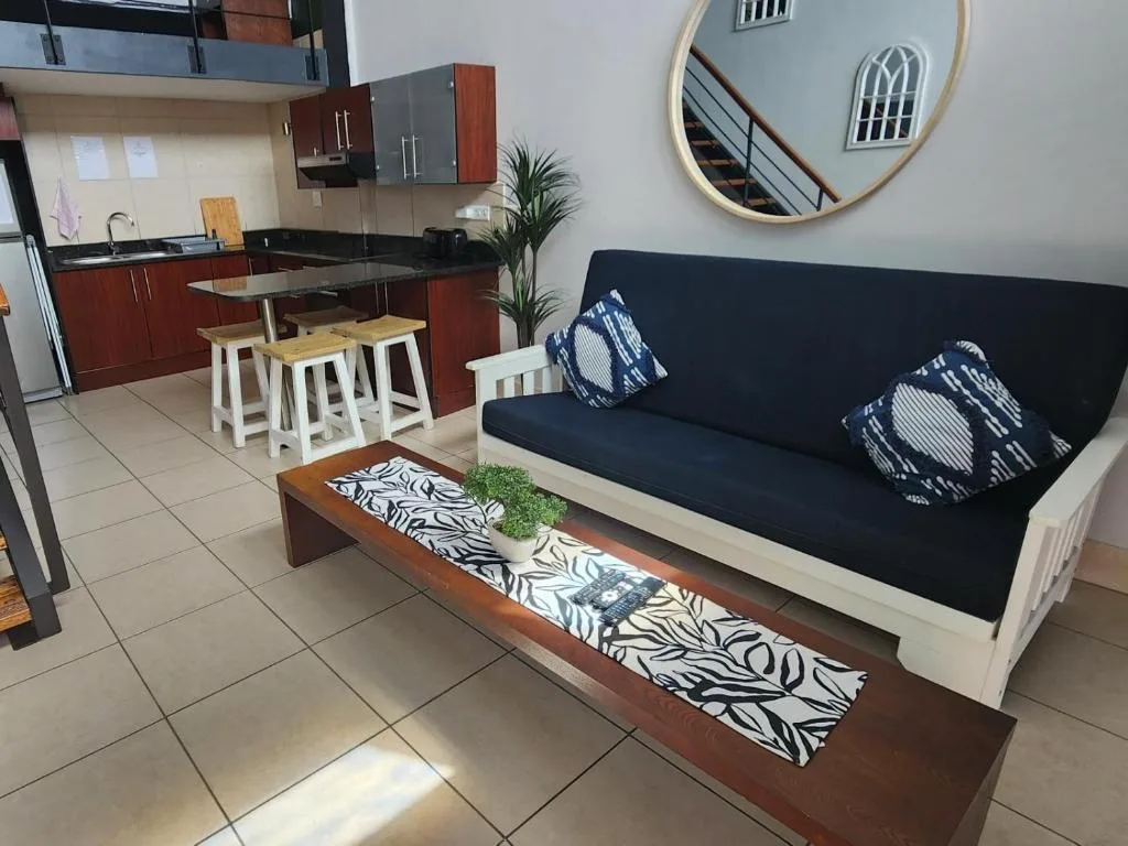 Open-plan lounge and kitchen with navy sofa, decorative cushions, and wooden coffee table