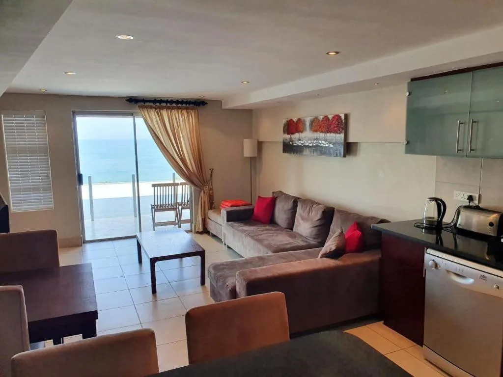 Modern lounge with grey sofas, red cushions, ocean view through glass doors