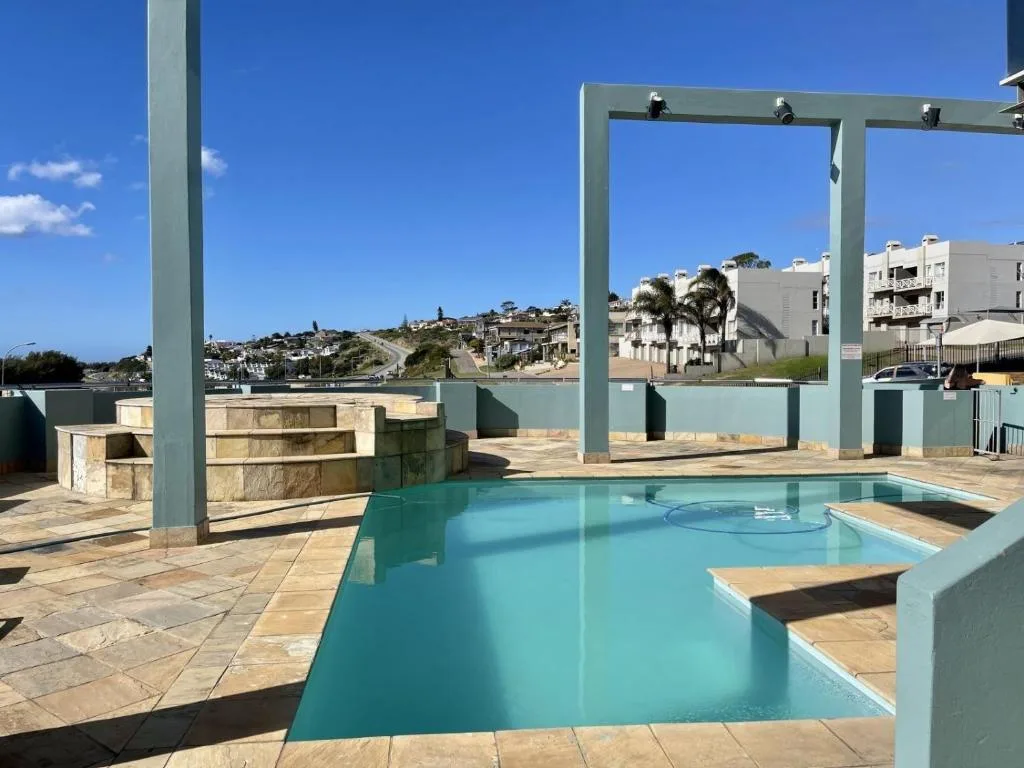Turquoise swimming pool with coastal town views and modern pergola structure