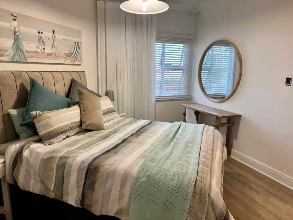 Spacious bedroom with striped bedding, coastal artwork, and round mirror