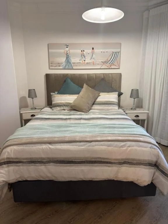 Modern bedroom with upholstered headboard, striped bedding, and coastal artwork