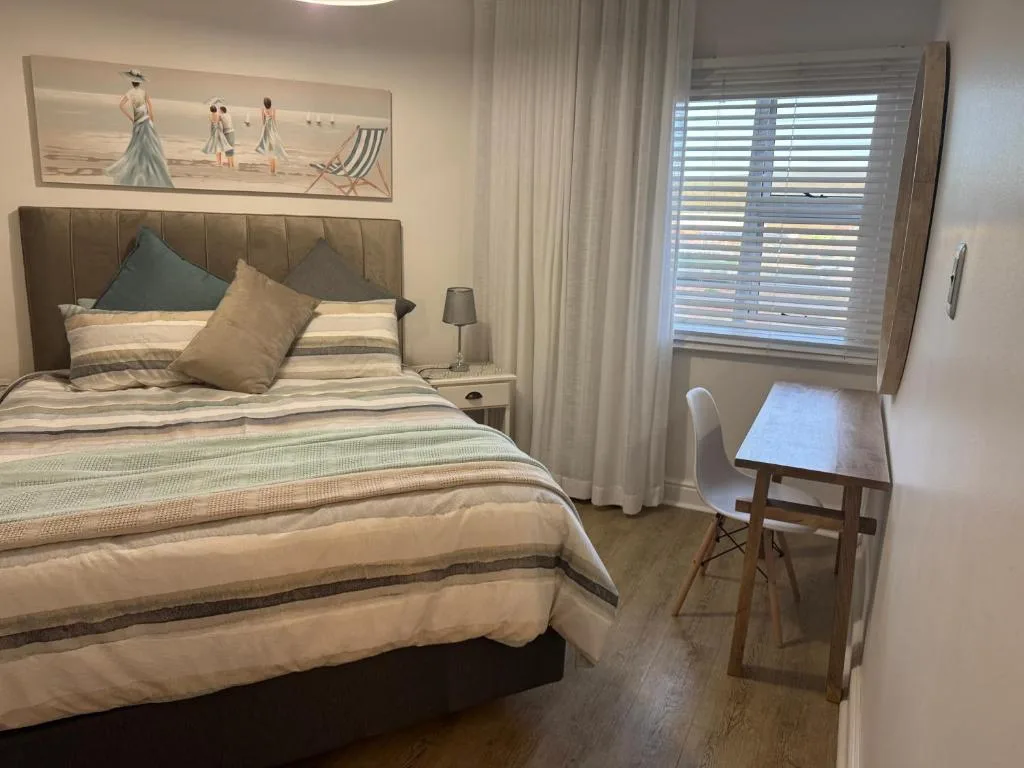 Spacious bedroom with upholstered headboard, striped bedding, and coastal artwork