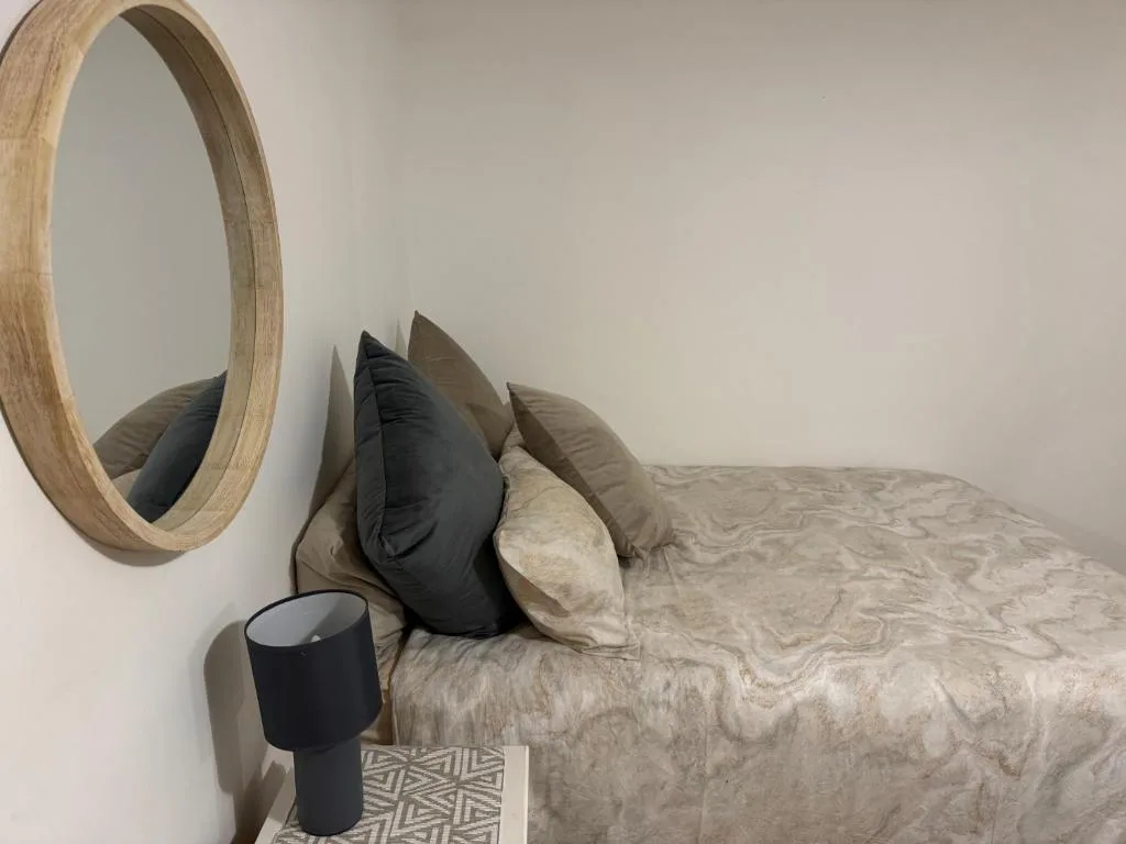 Minimalist bedroom with neutral bedding, decorative pillows, and round wooden mirror