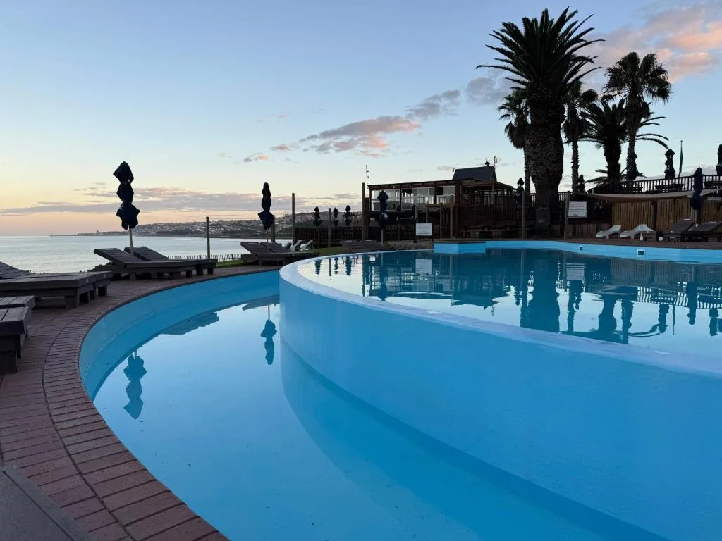 Curved lagoon-style pool overlooking calm ocean waters at sunset